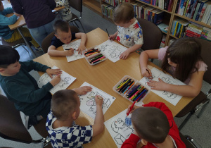 Chłopcy i dziewczynki kolorują ilustracje do bajki.