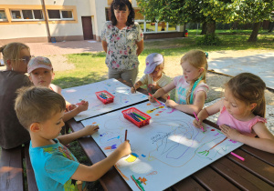 Dzieci z grupy "Słoneczek" malują przy stoliku na kartonie