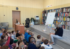 Dzieci oglądają ilustracje pokazywane przez prowadzącą.