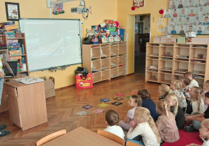 4.Dzieci siedzą przed tablicą i oglądają film z taśmy produkcyjnej fabryki pralek.