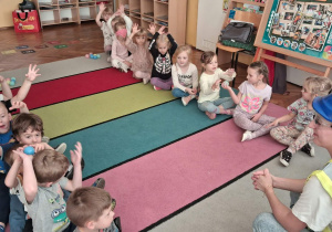7.Dzieci ćwiczą współpracę w taśmociągu siedząc w rzędach na dywanie.