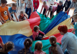 Krasnoludki krążą z chustą wokół siedzącej w środku „gniazda” małej Mai.