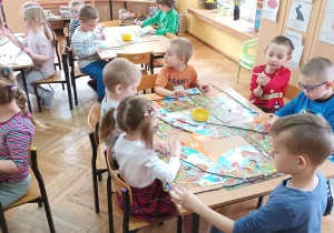 Dzieci próbują nakleić kolorowe pomponiki na gałązki.