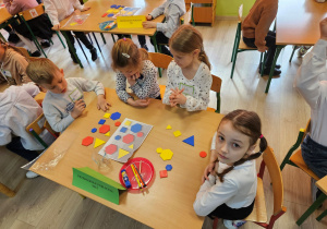 Szymon, Oliwia, Wiktoria i Zuzia siedzą przy stoliku i odzworowują obrazek z figur geometrycznych