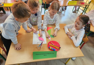 Szymon, Oliwia, Wiktoria i Zuzia siedzą przy stoliku i układają tangram królika