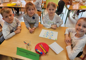 Szymon, Oliwia, Wiktoria i Zuzia siedzą przy stoliku zadowoleni, że skończyli układać obrazek z puzzli