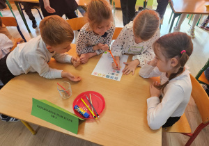 Szymon, Oliwia, Wiktoria i Zuzia siedzą przy stoliku i wykonują obliczenia na dodawanie i odejmowanie