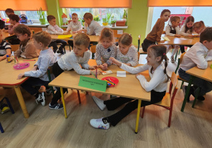 Szymon, Oliwia, Wiktoria i Zuzia siedzą przy stoliku i rozwiązują łamigłówkę