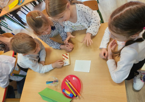 Szymon, Oliwia, Wiktoria i Zuzia siedzą przy stoliku i sprawdzają wynik zadania