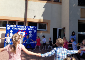 Przedszkolaki tańczą, trzymając się za ręce i tworząc duże koło.