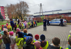 Dzieci witają policjantów na placu przedszkolnym.