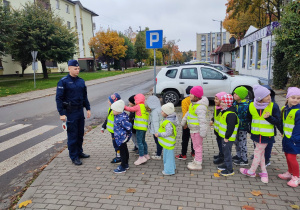 Policjant z dziećmi stoi przy pasach.