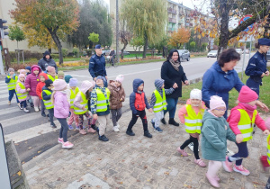 Dzieci w asyście policjanta bezpiecznie przechodzą po pasach.