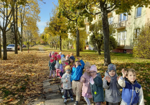 Przedszkolaki maszerują w parach i machają do wychowawcy.