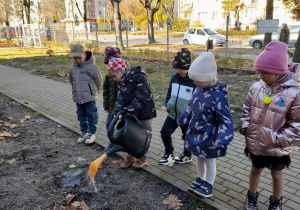 Dzieci przyglądają się jak Leon podlewa tulipany.