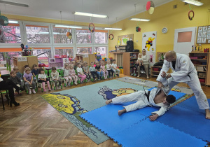 Dzieci siedzą i oglądają pokaz sztuki walki judo.