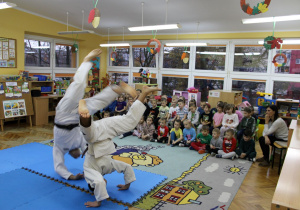 Dzieci siedzą i oglądają pokaz sztuki walki judo.