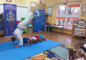 Sportowiec robi salto nad kucającymi dziećmi.