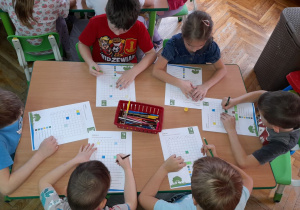 Dzieci rozwiązują zadania na kartach pracy.