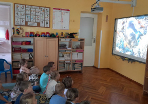 „Misiaczki” siedzą na dywanie i oglądają prezentację o zanieczyszczonych wodach oceanów.