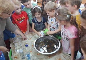 Antek przelewa zanieczyszczoną wodę do słoika z umocowaną na jego wierzchu gazą.