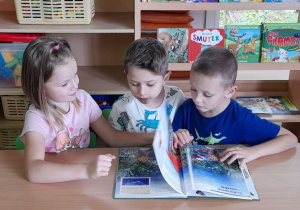 Dzieci siedzą przy stolikach i oglądają obrazki morskich zwierząt.