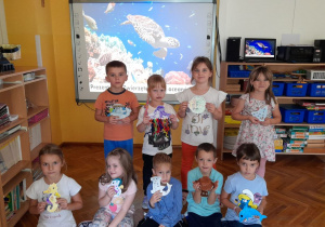 Przedszkolaki prezentują zwierzęta morskie, wykonane z materiałów plastycznych.