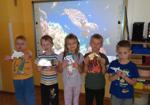 Przedszkolaki prezentują zwierzęta morskie, wykonane z materiałów plastycznych.