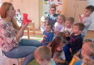 Prowadząca pokazuje dzieciom kalosze wydrukowane na drukarce 3D.