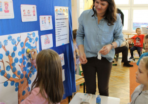 Pani Ewelinka asystuje dzieciom podczas tworzenia ,,drzewa”.