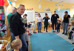 Rodzice wraz z dziećmi stoją w kole i wykonują ruchy do zabawy muzycznej