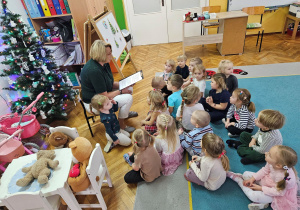 Pani Ania czyta bajkę o Świętym Mikołaju a dzieci siedzą na dywanie