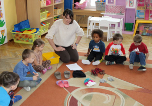 Dzieci siedzą na dywanie i oglądają przedmioty przyniesione przez panią.