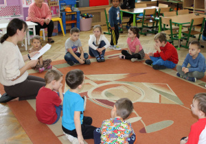 Dzieci siedzą na dywanie i słuchają bajki terapeutycznej o pajączku.