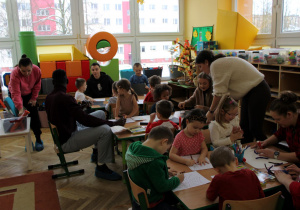 Rodzice z dziećmi pracują przy stolikach.