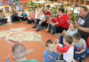 Rodzice z dziećmi bawią się na dywanie w zabawę ruchową.