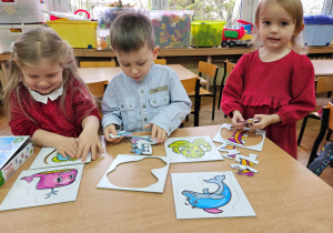 Kornelia, Jaś i Julia z grupy "Biedronki" układają przy stoliku nowe puzzle