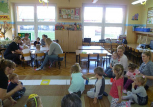  Dzieci przy stole kolorują obrazki i ozdabiają dużą grę planszową, pomaga mama Julki;