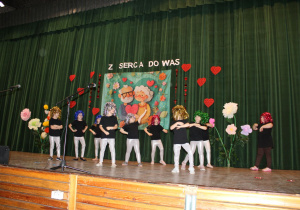 Dziewczynki z koła tanecznego w kolorowych perukach na głowie tańczą do kolejnego utworu.