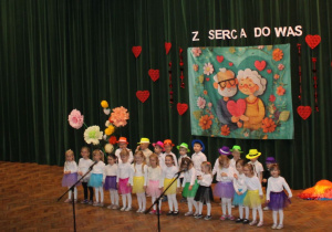 Dziewczynki i chłopcy z grupy „Słoneczek” wesoło prezentują się podczas śpiewu „Piosenki dla Babci i Dziadka”.