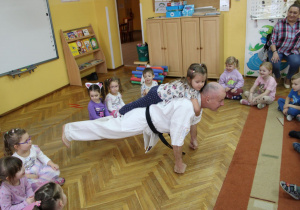 Pan Arek wykonuje pompki z obciążeniem – na jego plecach siedzi Łucja.