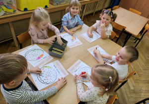 Dzieci kolorują przy stoliku malowankę pączka