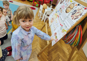 Wiktoria wskazuje palcem pasujący pączek do zagadki