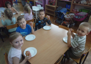 Dzieci jedzą przy stoliku słodkie pączki
