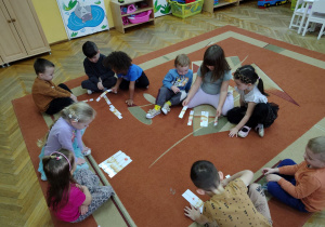 Dzieci układają pączkowe puzzle na dywanie.