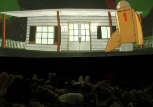 Dzieci leżą w mobilnym planetarium i obserwują start rakiety, wykonanej z kartonu.