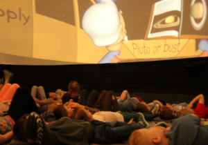 Przedszkolaki wsłuchują się w opowieść i obserwują planety na ekranie.