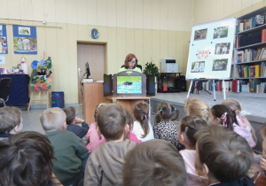 Pani Ilona siedzi i przedstawia dzieciom ilustracje teatrzyku kamishibai.