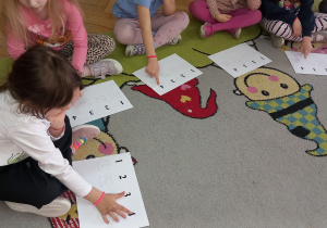 Dziewczynki wodzą palcami po wzorze na kartkach.