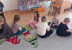 Dzieci scedzą na dywanie na przeciwko siebie w parach i podają sobie woreczek.